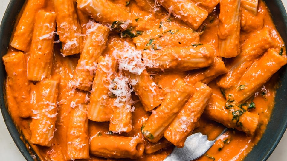 pink sauce Tortiglioni in a bowl with a fork, sprinkled with grated parmesan cheese and fresh chopped basil