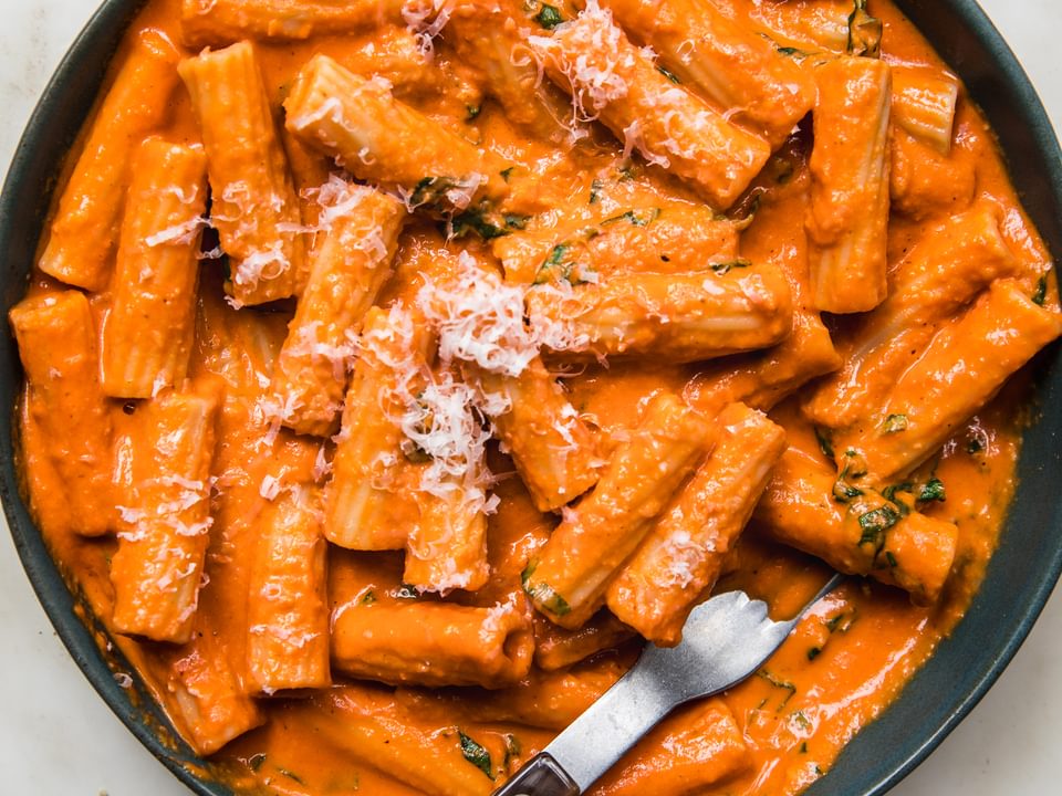 pink sauce Tortiglioni in a bowl with a fork, sprinkled with grated parmesan cheese and fresh chopped basil