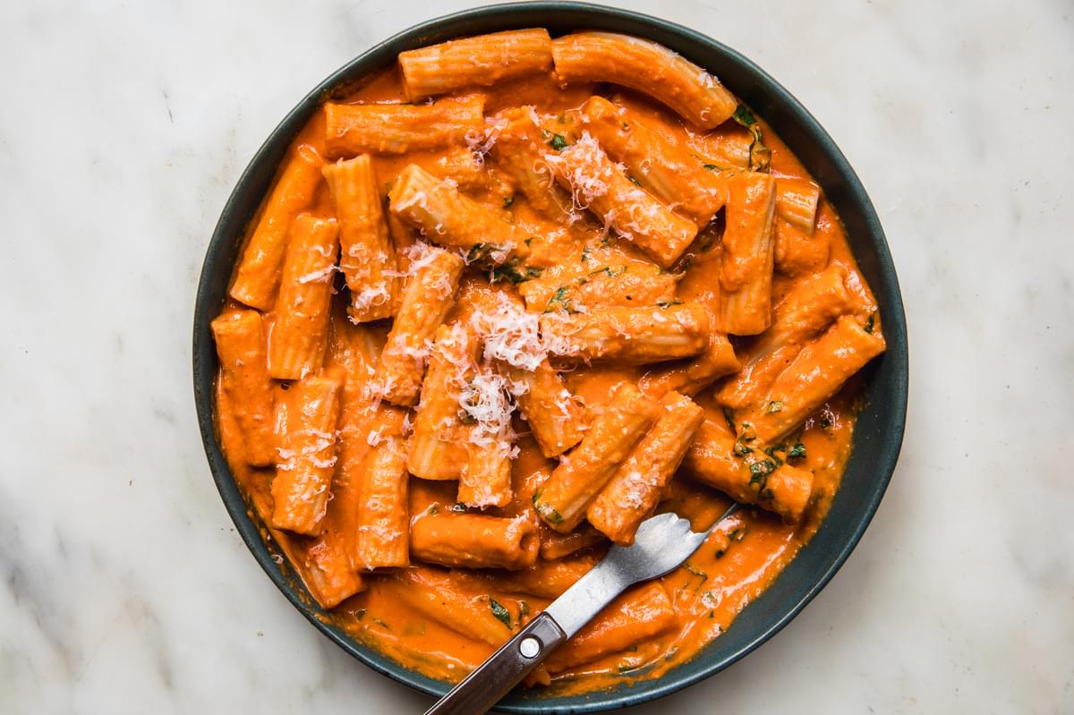 a bowl of pink sauce Tortiglioni pasta topped with parmesan and fresh basil with a fork in it