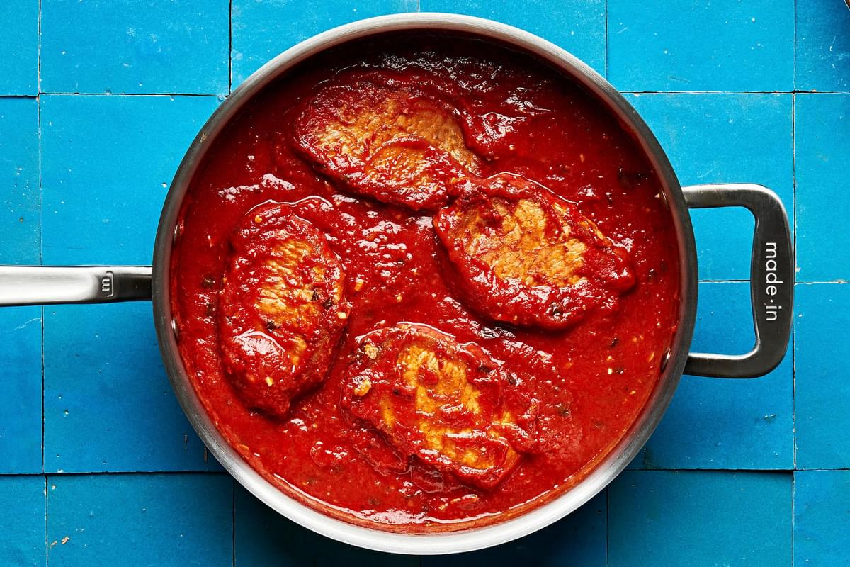 4 pork chops braised in tomato sauce in a skillet