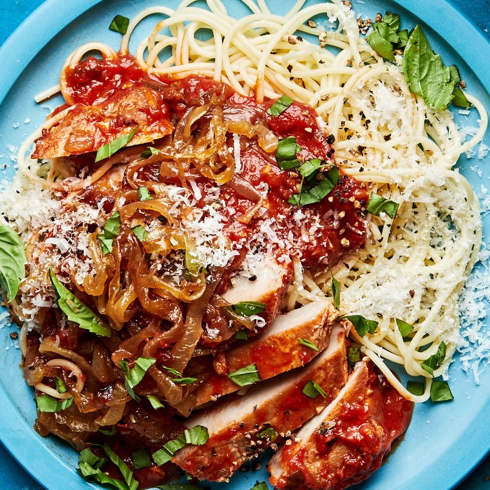 pork chops braised in tomato sauce served on cooked pasta noodles and topped with caramelized onions, basil and parmesan
