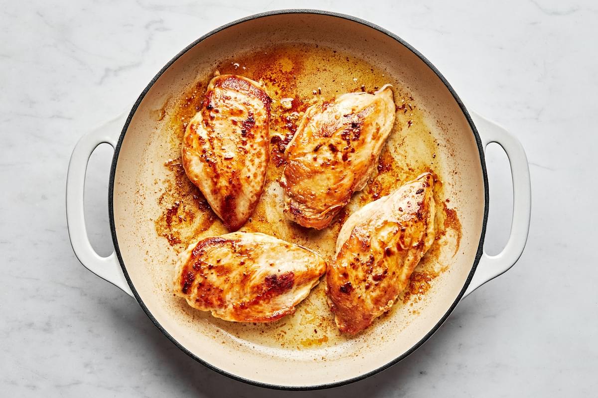 salted chicken breast being browned in a pan with olive oil