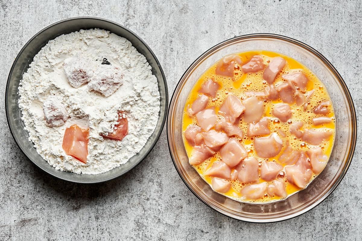 raw chicken breast bites being dipped into a bowl of beaten egg and then rolled in a bowl flour and cornstarch