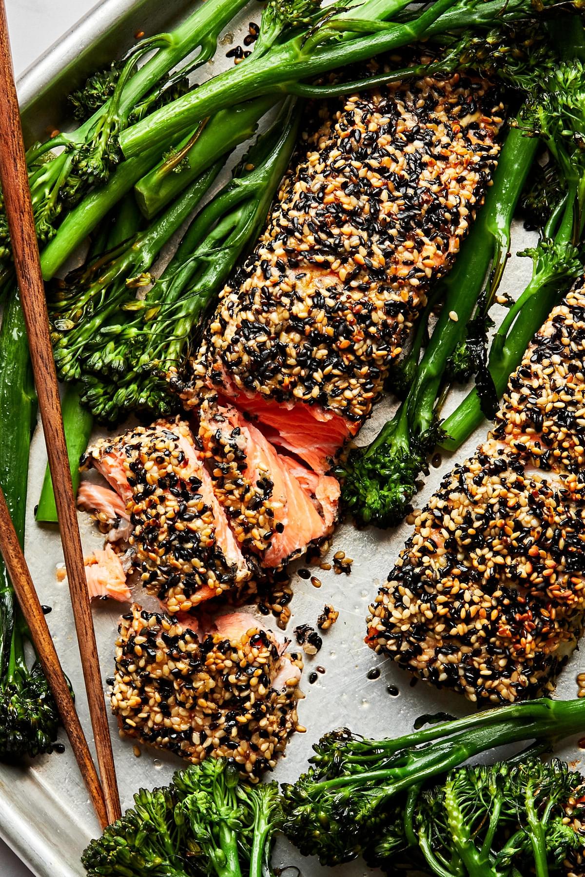 Sesame crusted salmon and roasted broccolini on a baking sheet with chop sticks