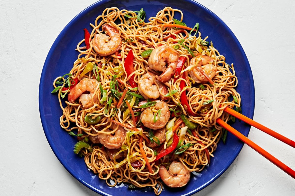 shrimp chow mein made with soy sauce, chili sauce, ginger, garlic, sesame oil and vegetables on a plate with chopsticks