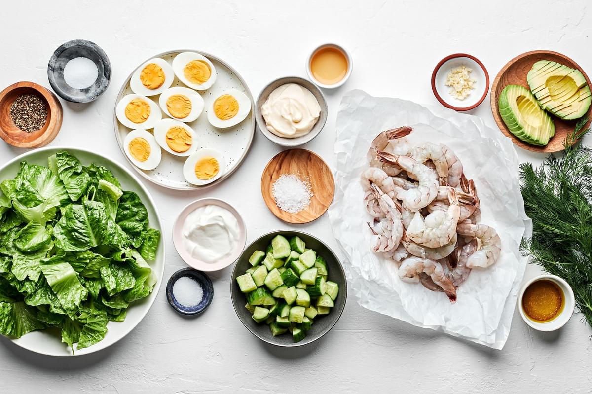romaine, cucumbers, hard boiled eggs, avocado, shrimp and ingredients for dill dressing in prep bowls on the counter