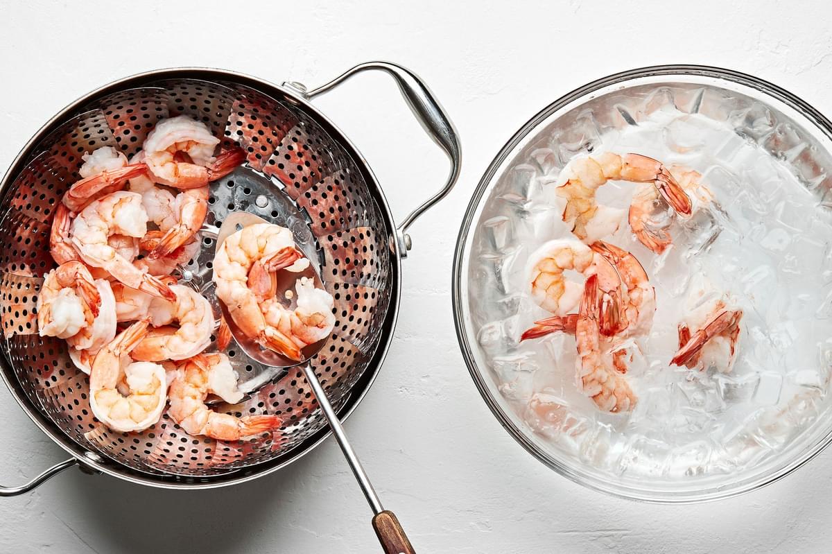 cooked shrimp in a steamer being transferred to an ice bath with a slotted spoon
