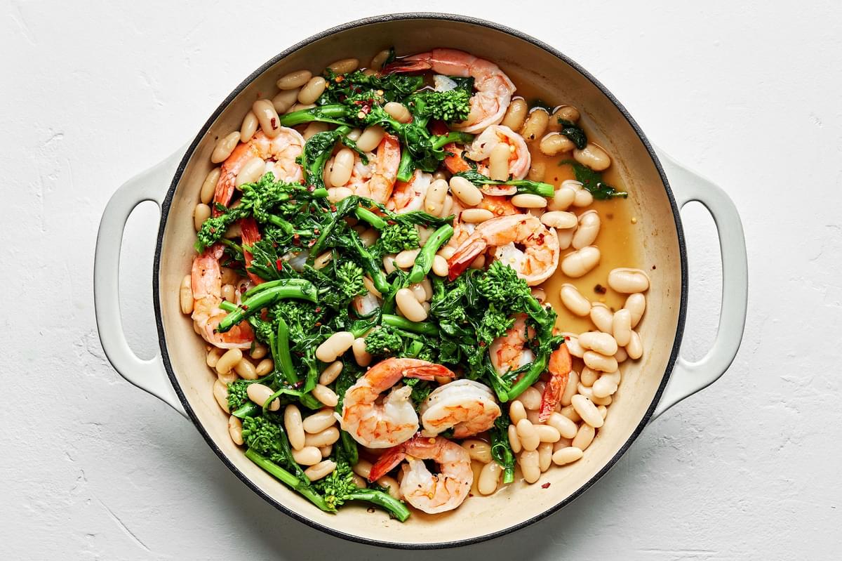 shrimp, broccoli rabe, white beans salt, pepper, red pepper flakes and chicken broth cooking in a skillet