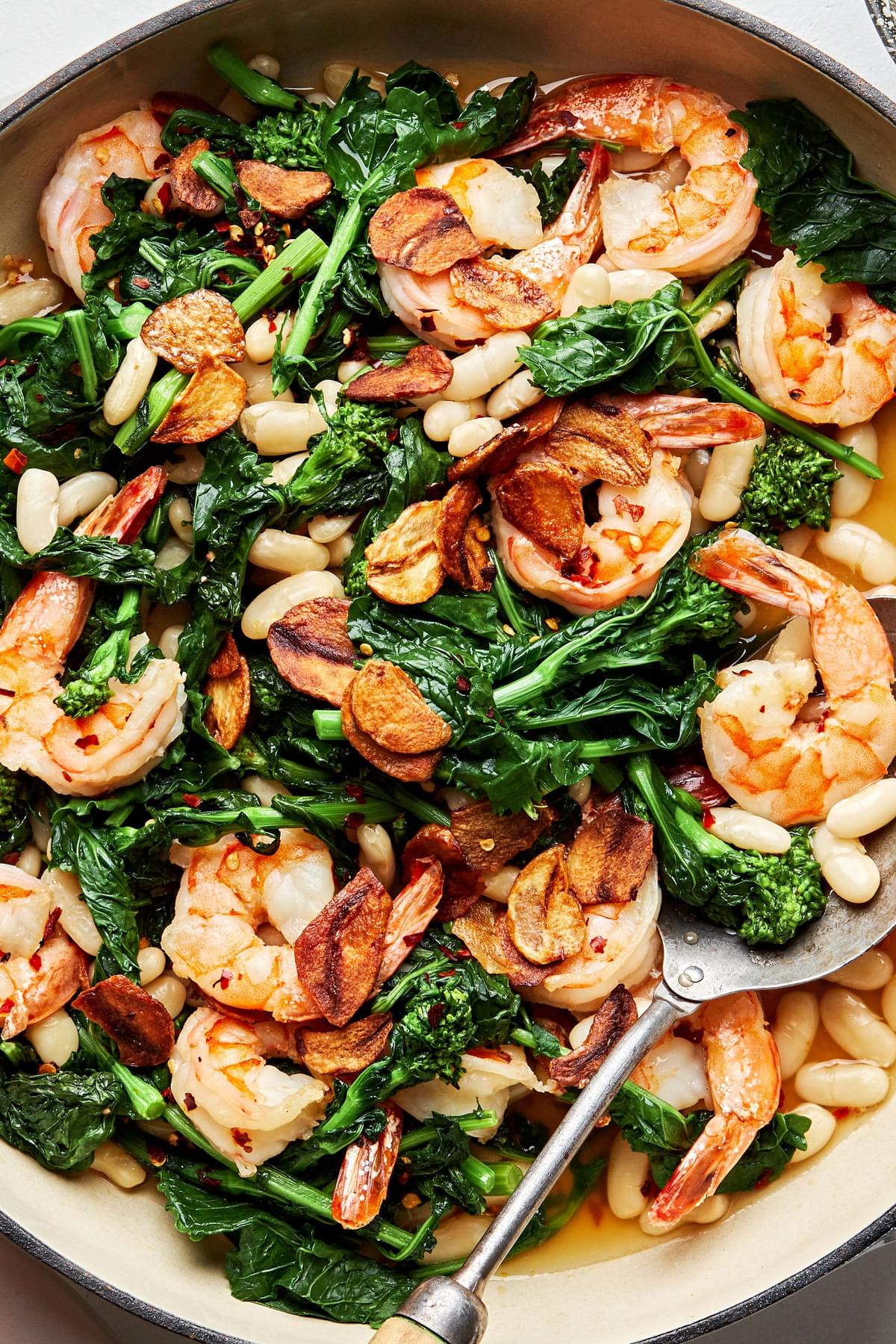 Spicy Broccoli Rabe with White Beans and Shrimp in a pan with a serving spoon