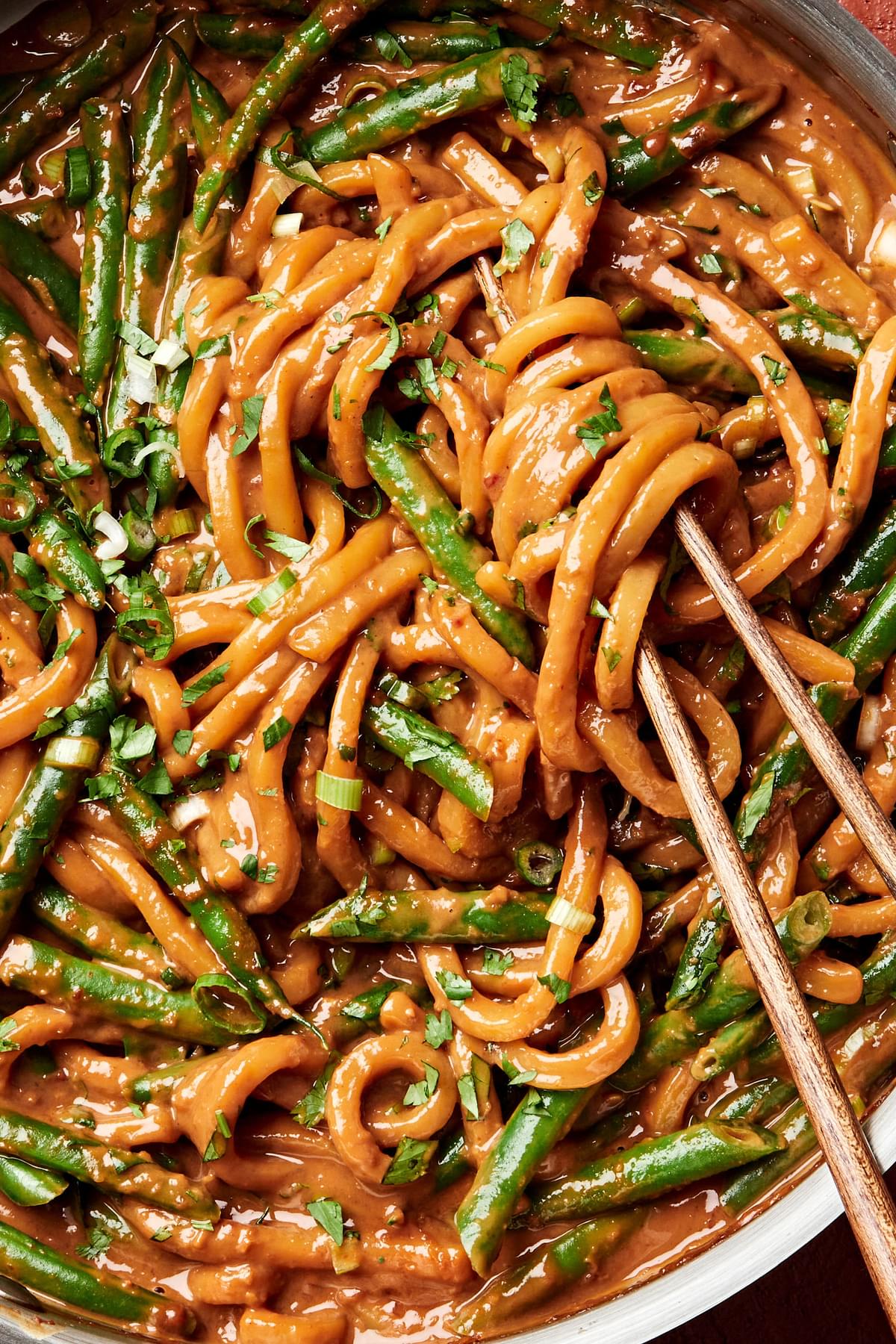 homemade spicy peanut udon noodles tossed with green beans being stirred with chopsticks