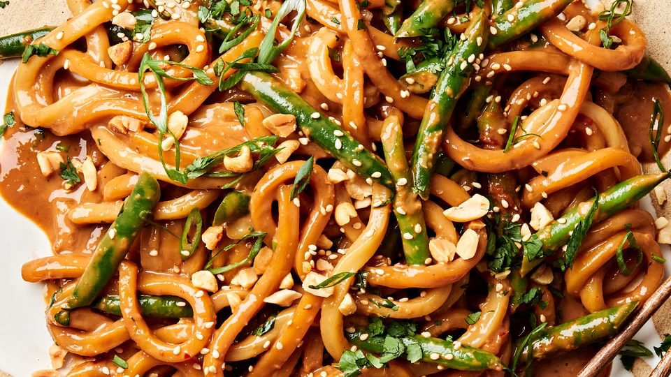 homemade spicy peanut udon noodles topped with green onions, cilantro, sesame seeds, and crushed peanuts on a plate