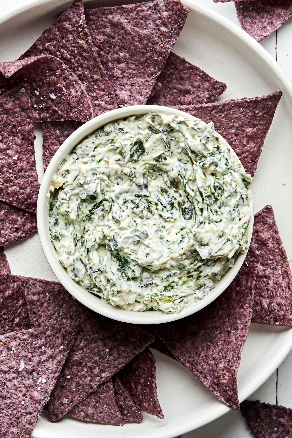a bowl of homemade spinach dip surrounded by blue corn tortilla chips for dipping