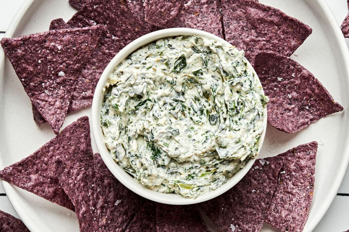 a bowl of homemade spinach dip surrounded by blue corn tortilla chips for dipping
