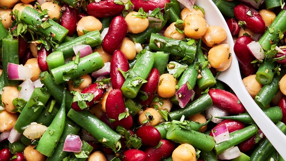 3 bean salad in a serving bowl with a serving spoon made with green beans, kidney beans, garbanzo beans, red onion & parsley
