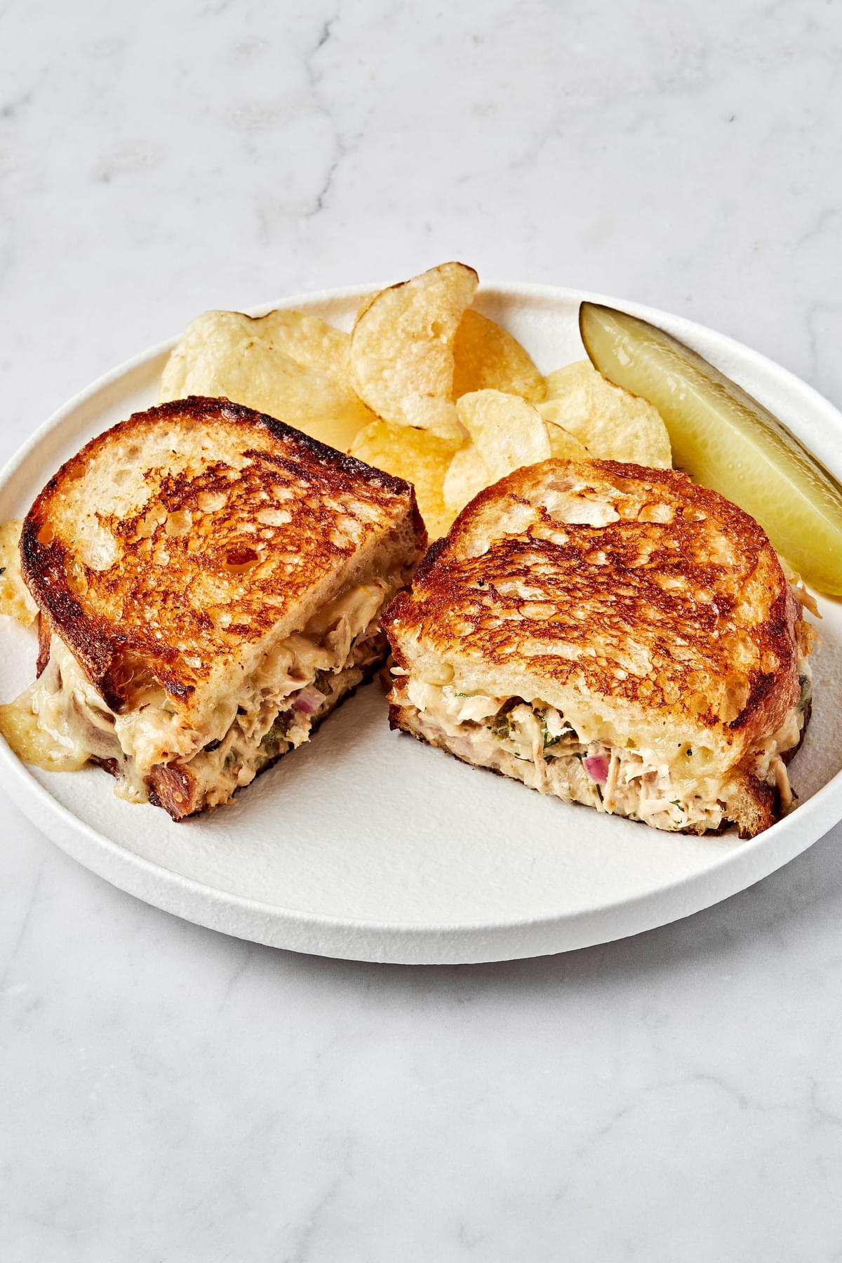 a homemade tuna melt sandwiched cut in half and stacked on a plate surrounded by potato chips