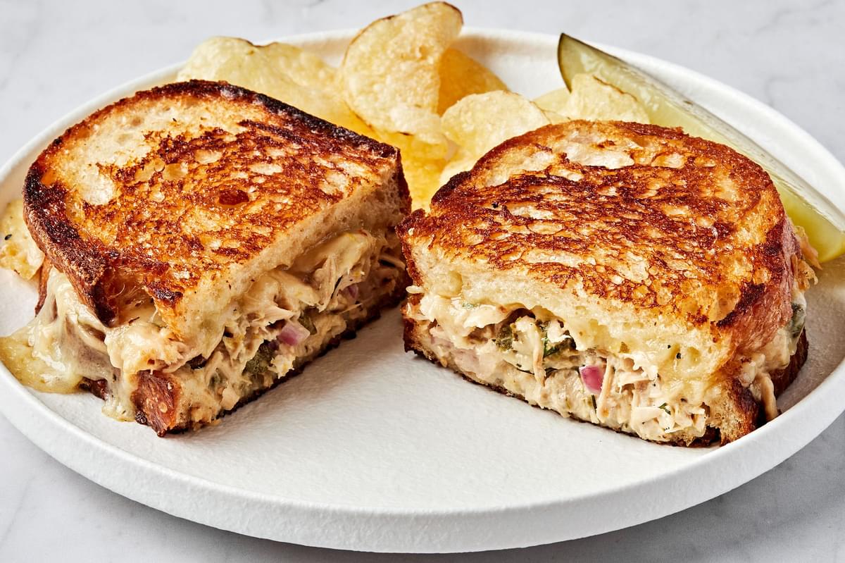 a homemade tuna melt sandwiched cut in half and stacked on a plate surrounded by potato chips