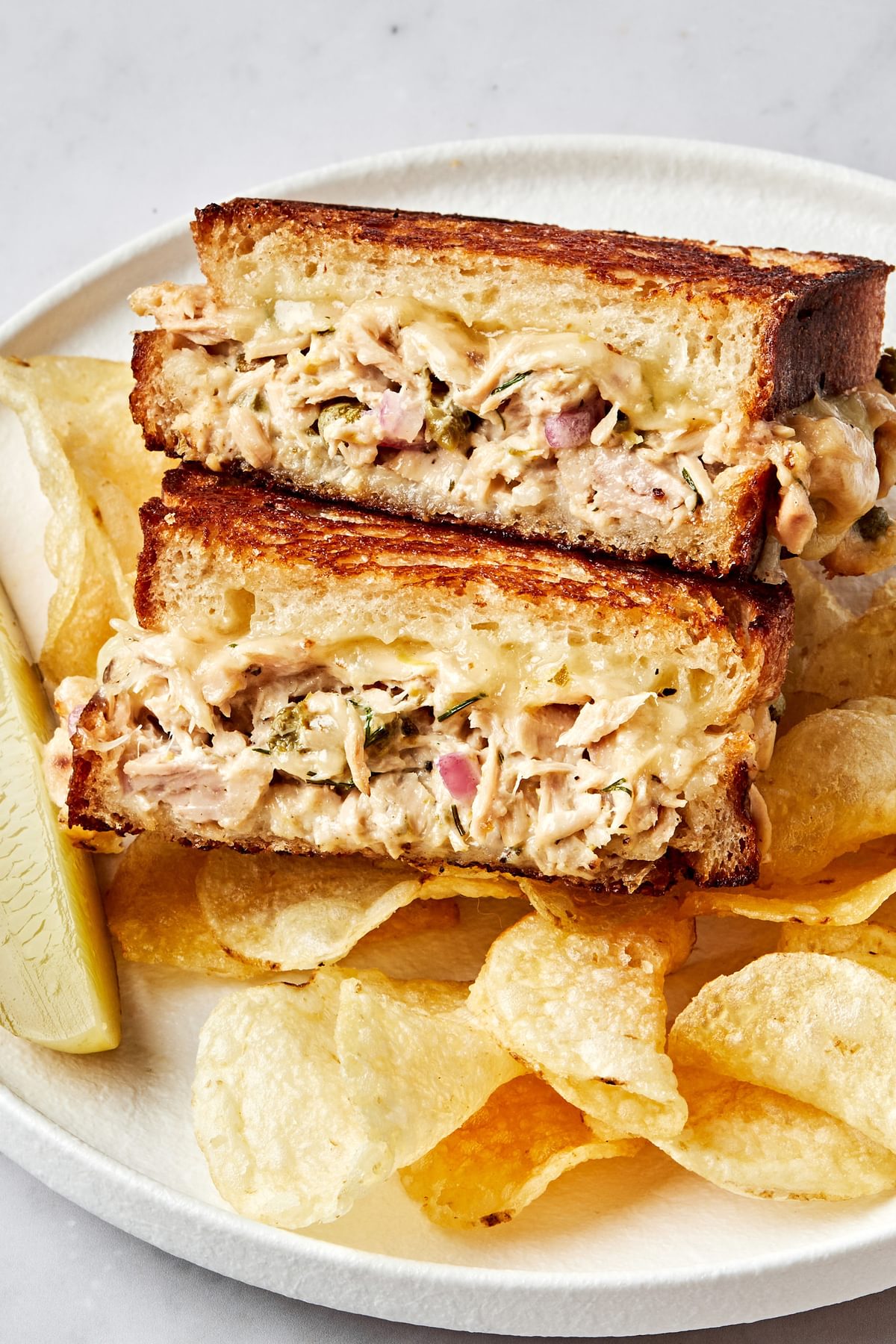 a golden brown tuna melt sandwiched cut in half and stacked on a plate surrounded by potato chips