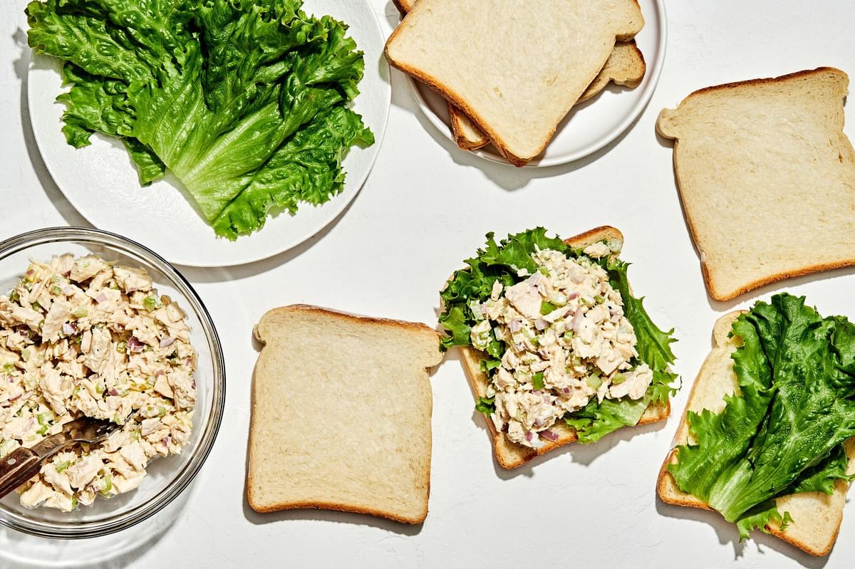 slices of bread on a counter being topped with lettuce and homemade tuna salad