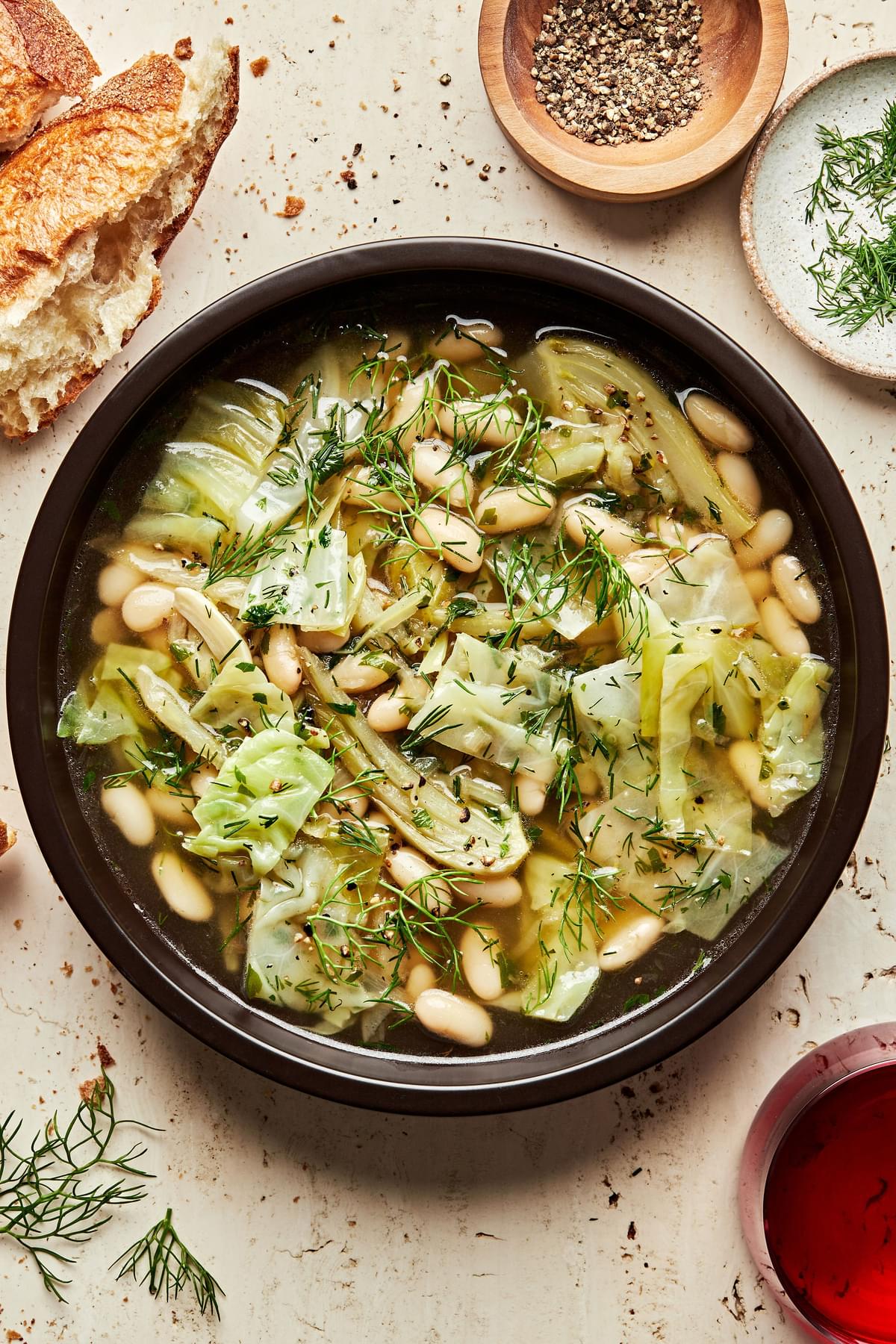 a bowl White Bean Soup with Dill and Cabbage being served with crusty bread