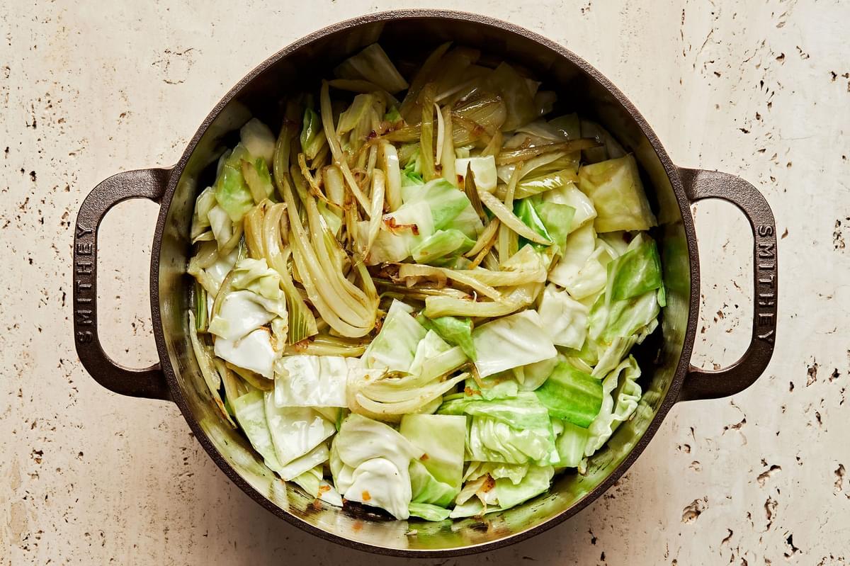 shallots, fennel, salt, cabbage and garlic being cooked in olive oil in a large soup pot