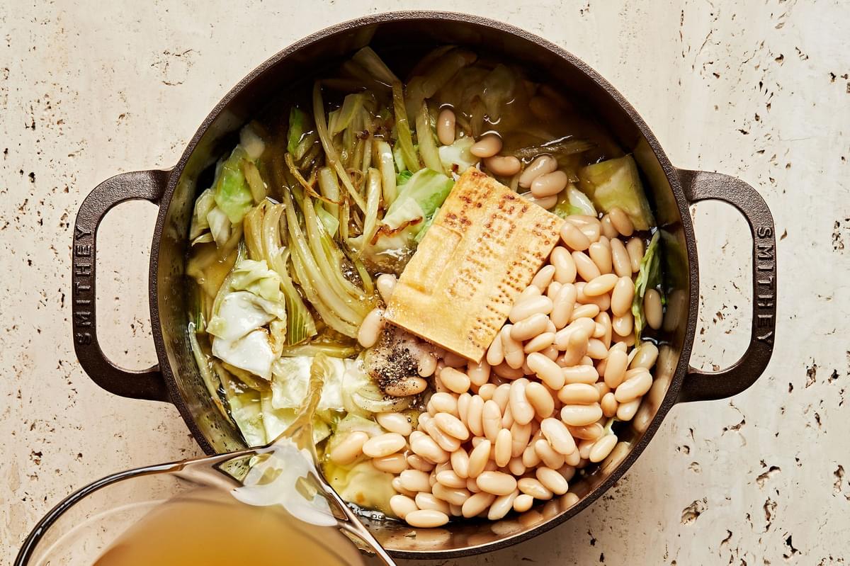 stock, beans, parmesan rind, shallots, fennel, salt, cabbage and garlic being cooked in olive oil in a large soup pot