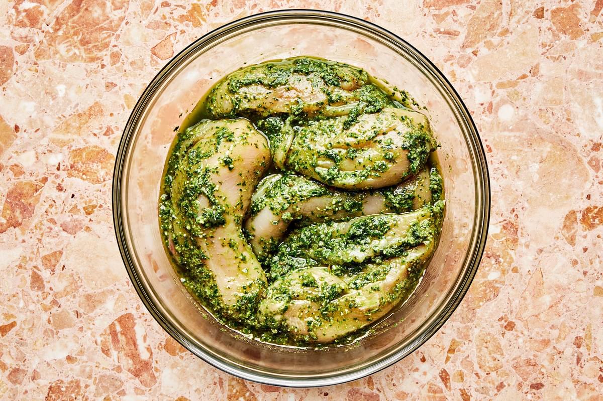 chicken being coated in pesto sauce in a glass bowl