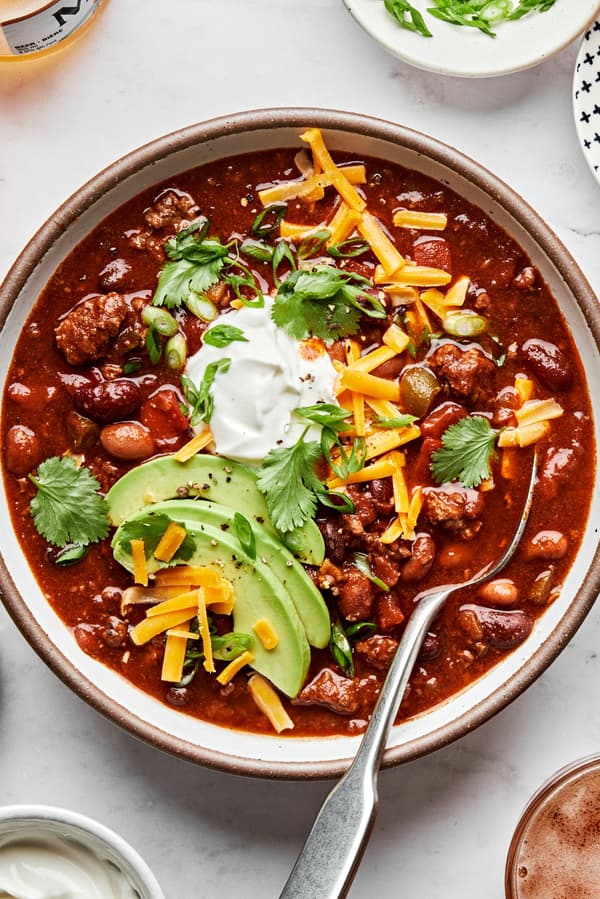 a bowl of homemade chili made with beef, pork, kidney, black and pinto beans topped with cheese, sour cream and avocado