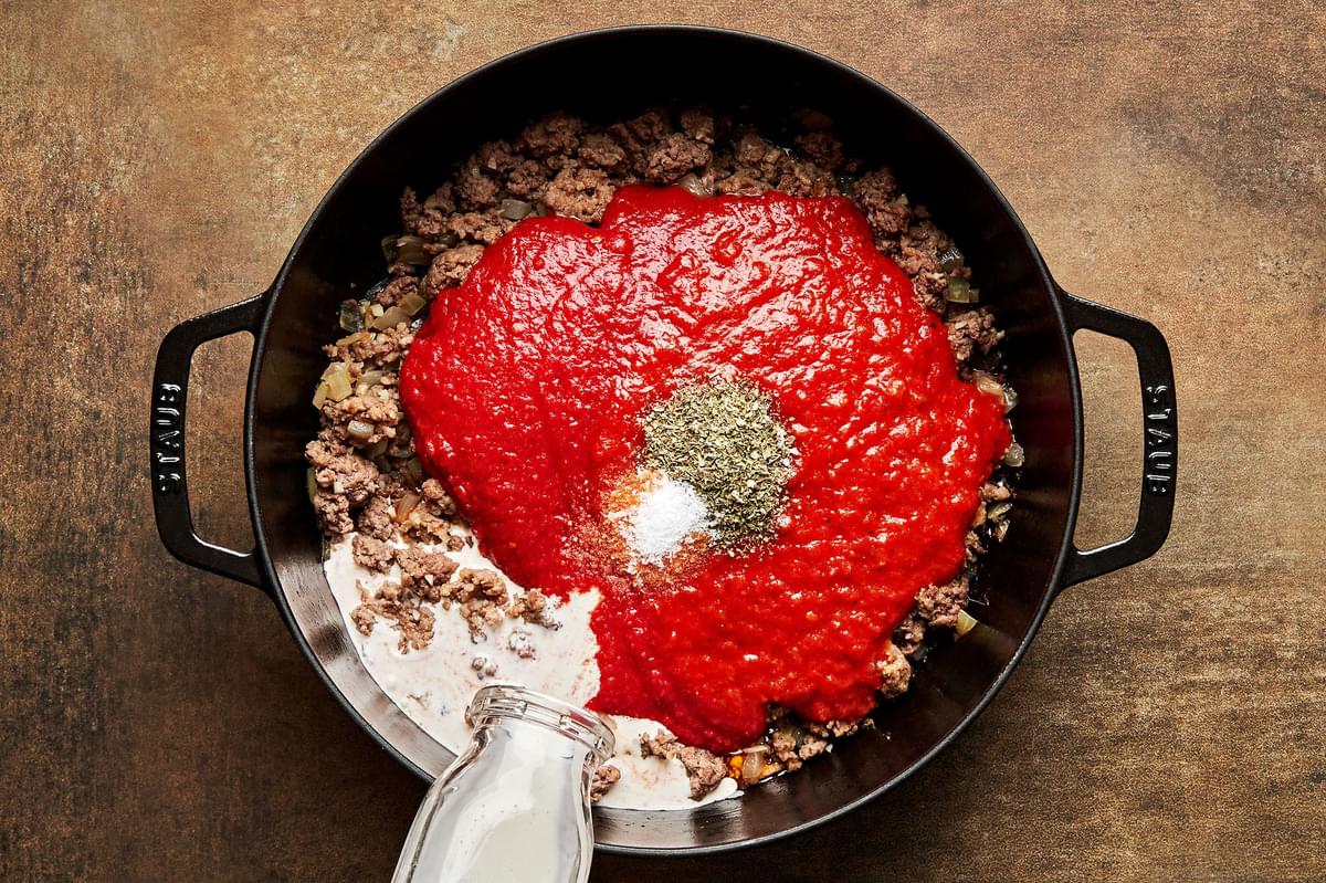 marinara, crushed tomatoes, salt, Italian seasoning & cream being added to a pot with Italian sausage, beef and onions