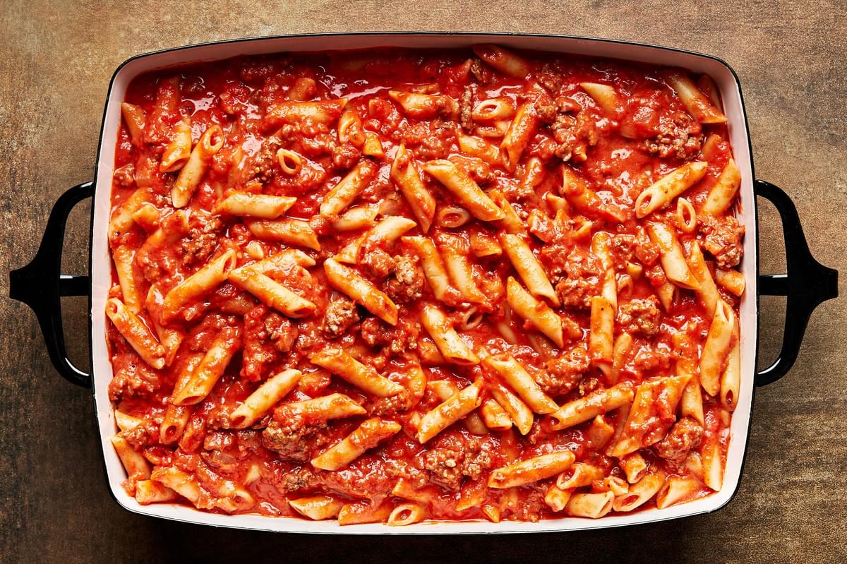 Cooked Mostaccioli and pasta sauce being spread into a 9x13 baking pan