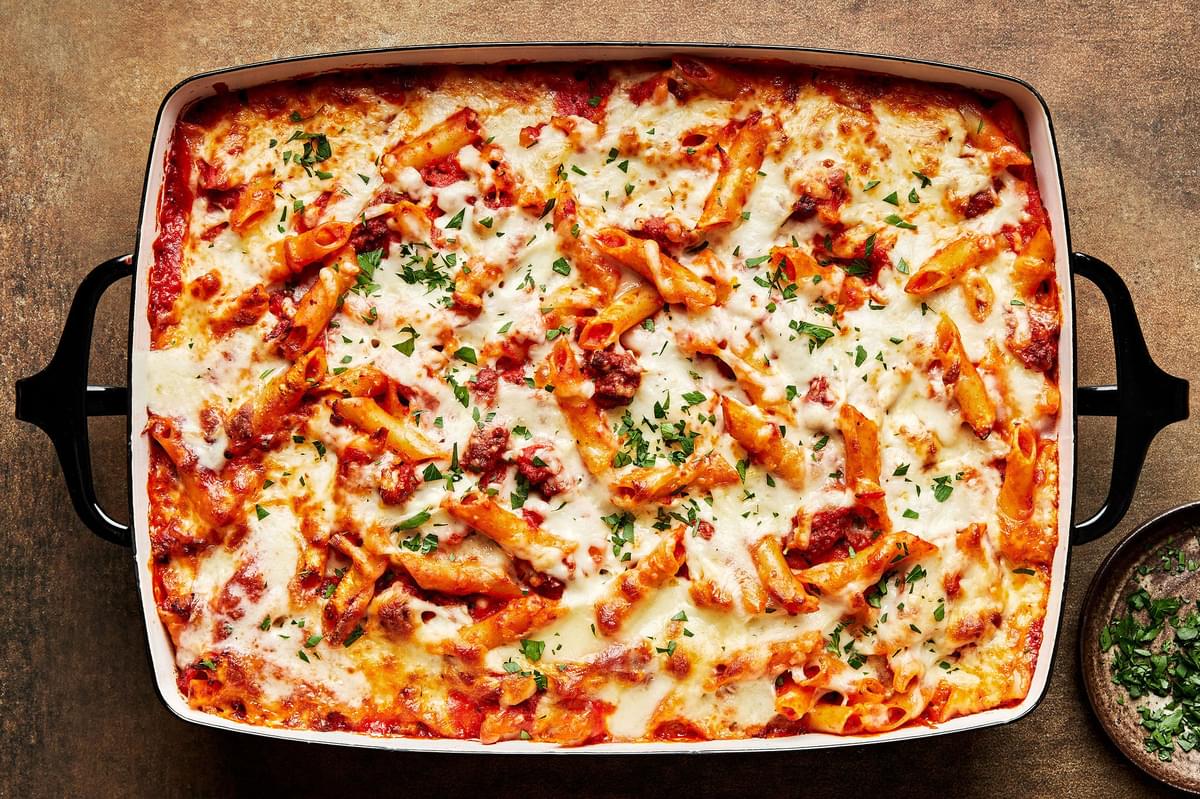 homemade baked Mostaccioli topped with melted mozzarella cheese and sprinkled with parsley in a 9x13 baking pan