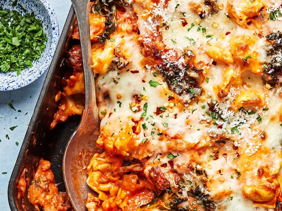 baked tortellini being scooped out of a baking dish made with Italian sausage ad mozzarella