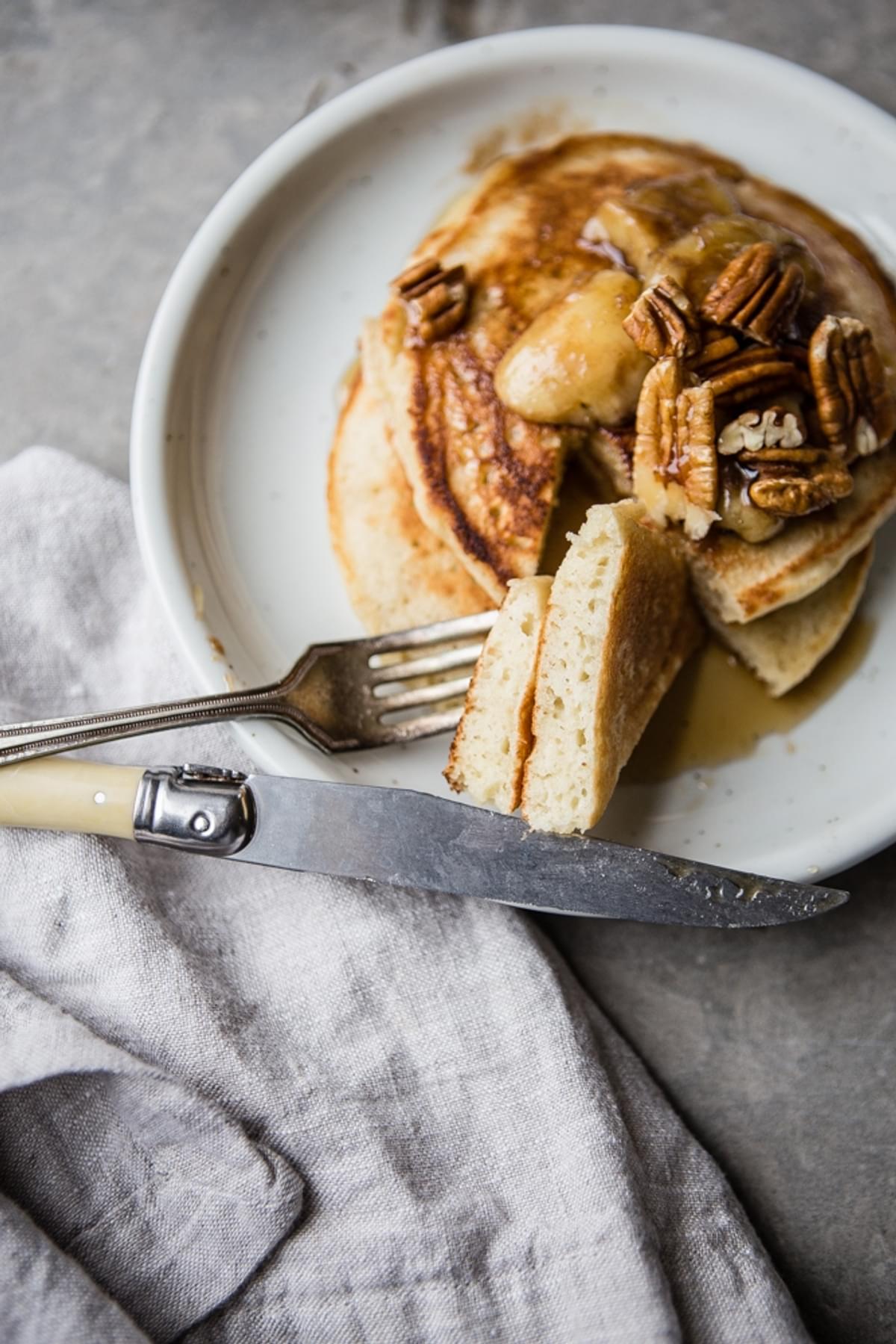 a plate of Pancakes with Caramelized Bananas and Toasted Pecans with a piece taken out