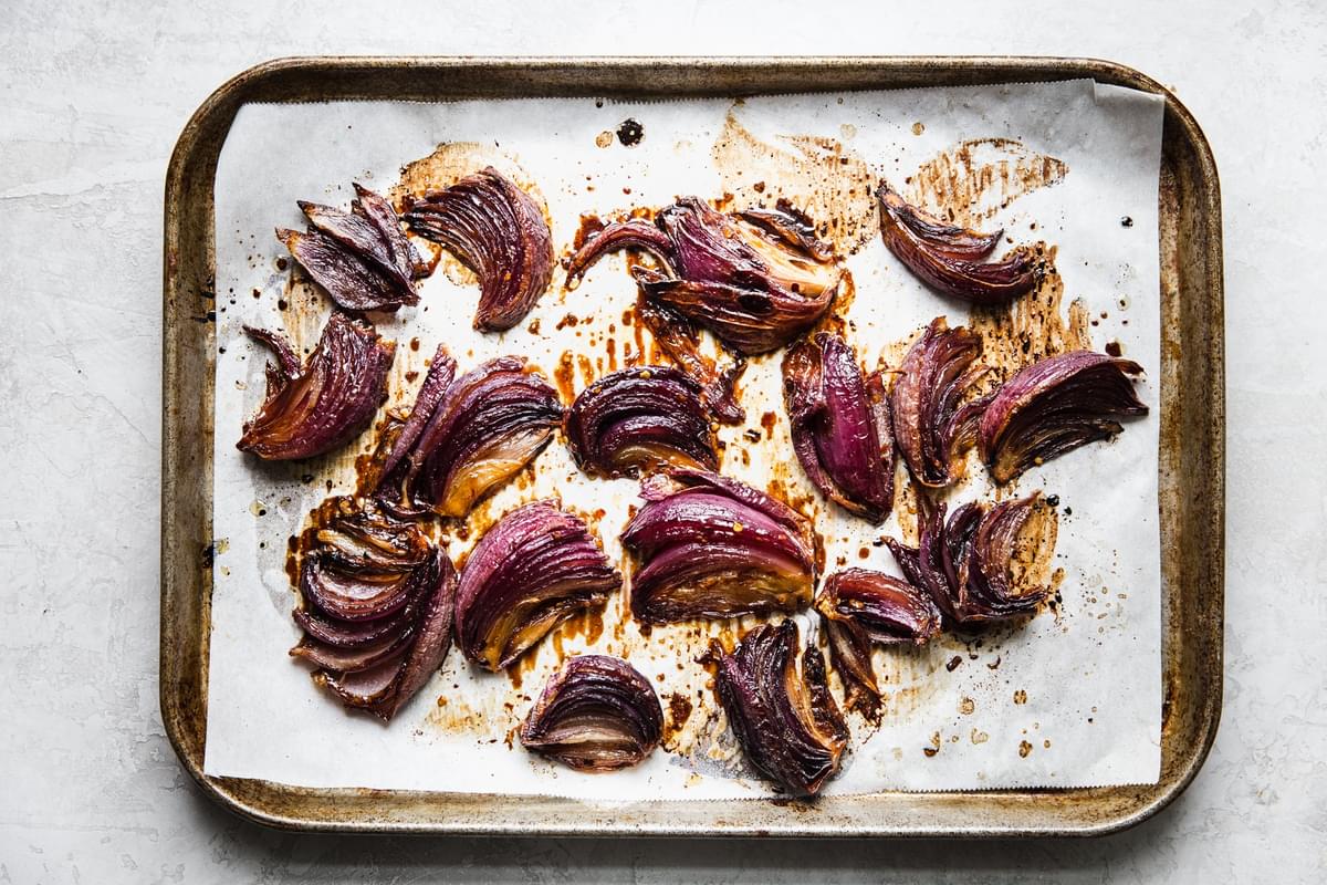 roasted red onions on a baking sheet seasoned with brown sugar, red pepper flakes, olive oil, balsamic vinegar and salt