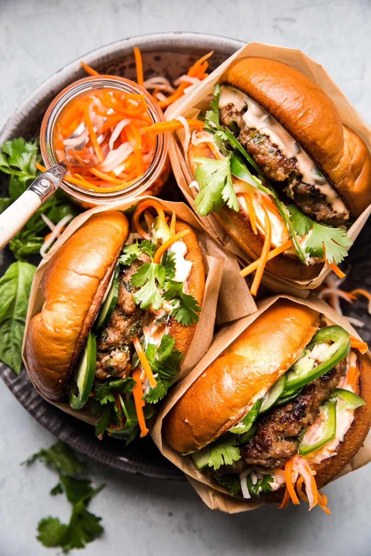 3 pork banh mi burgers on a plate with pickled veggies, cilantro and basil