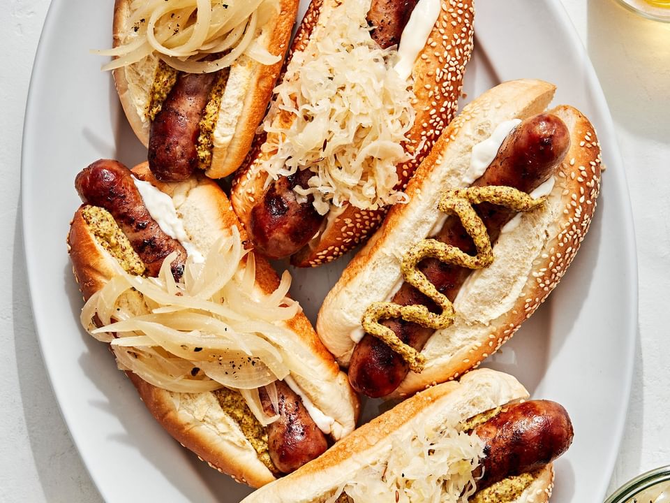 a platter of beer brats served on hoagie rolls topped with sauerkraut, onions, mustard and mayo