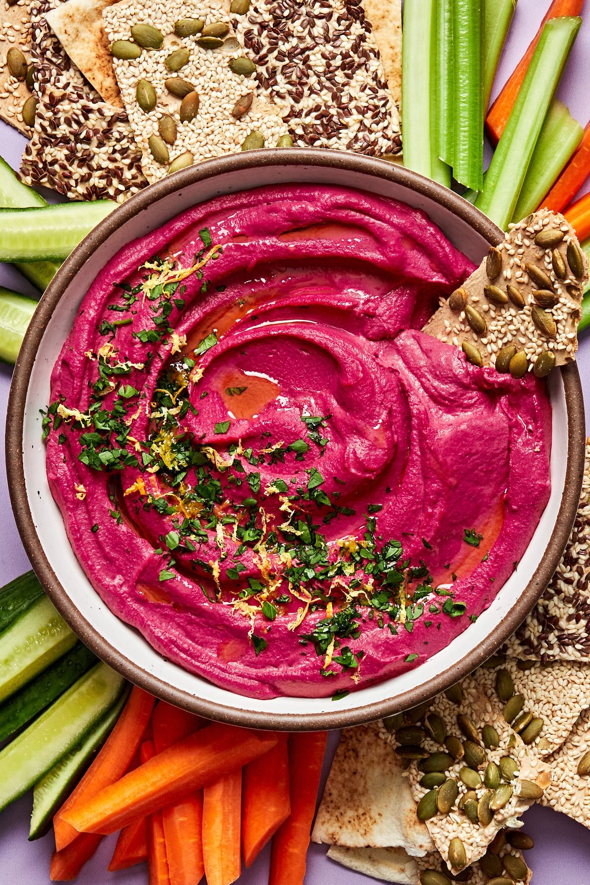 homemade beet hummus in a serving bowl surrounded by crackers, celery and carrots for dipping