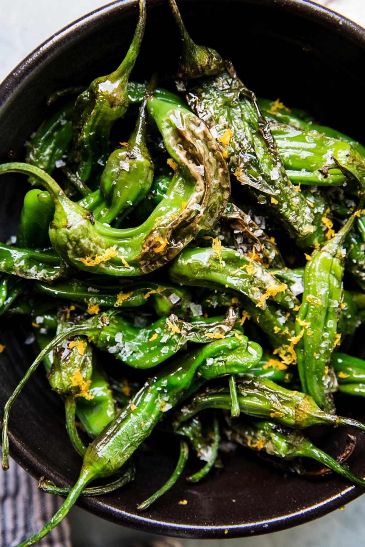 Blistered Shishito Peppers in olive oil, sea salt and lemon zest in a black bowl