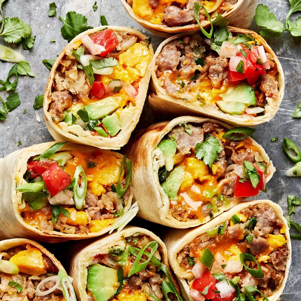 breakfast burritos sliced in half filled with potatoes, eggs, sausage, green onions, cheddar, avocado, salsa and cilantro