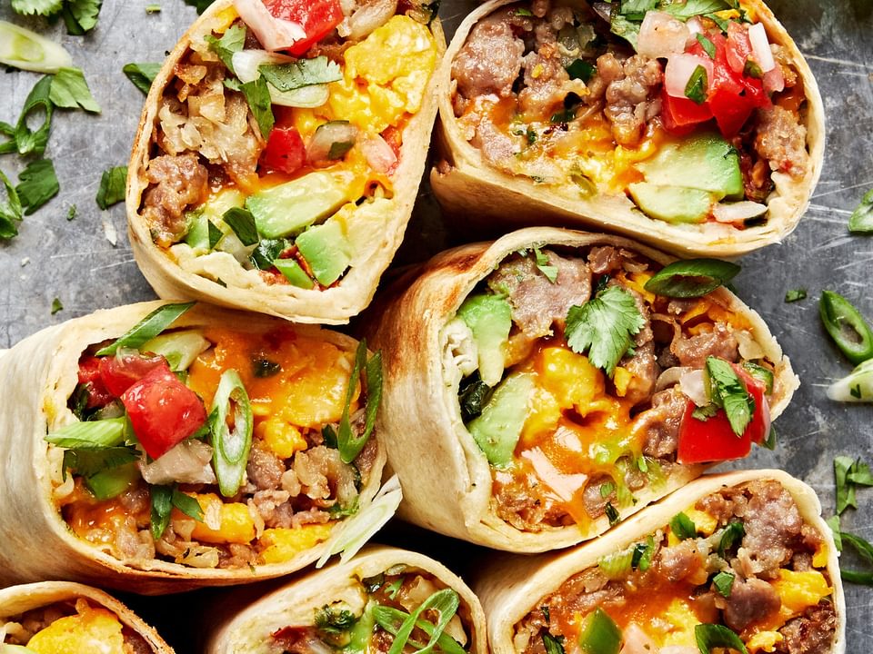breakfast burritos sliced in half filled with potatoes, eggs, sausage, green onions, cheddar, avocado, salsa and cilantro