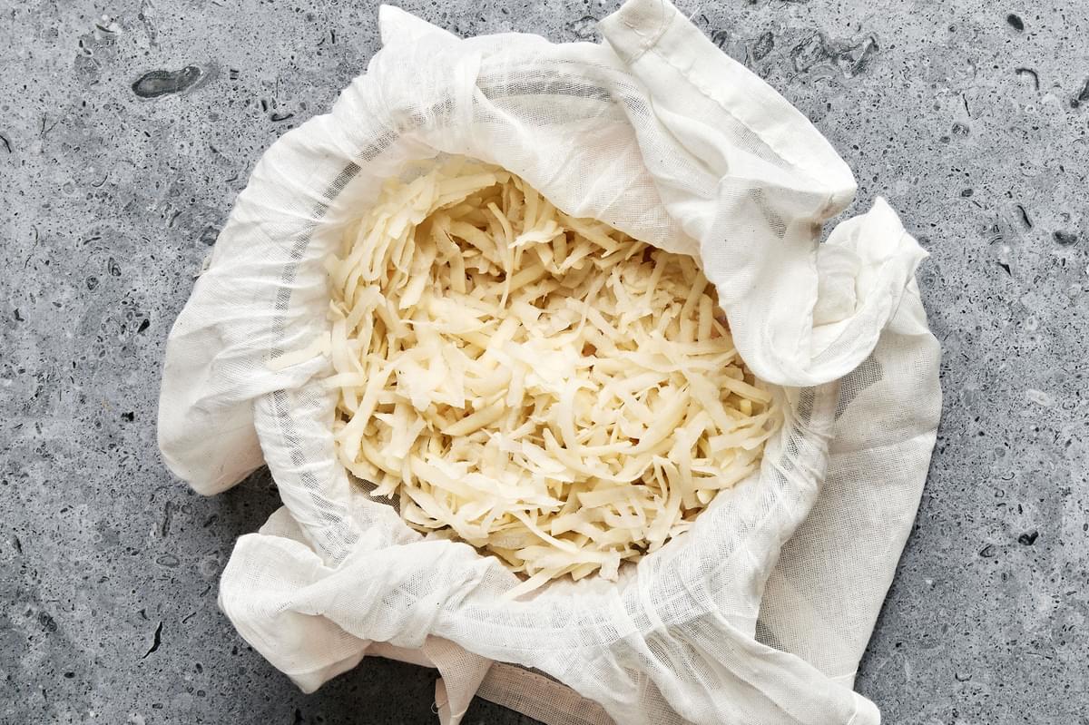 shredded potatoes being squeezed in cheesecloth to remove moisture