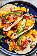 breakfast tacos made with eggs, bacon, cilantro, sliced avocado, pico de gallo, and a squeeze of lime juice & hot sauce