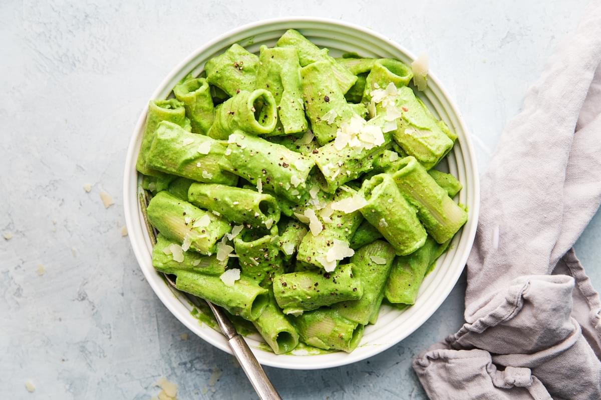 Rigatoni pasta with broccoli pesto in a bowl with a spoon with parmesan and one nuts with a spoon