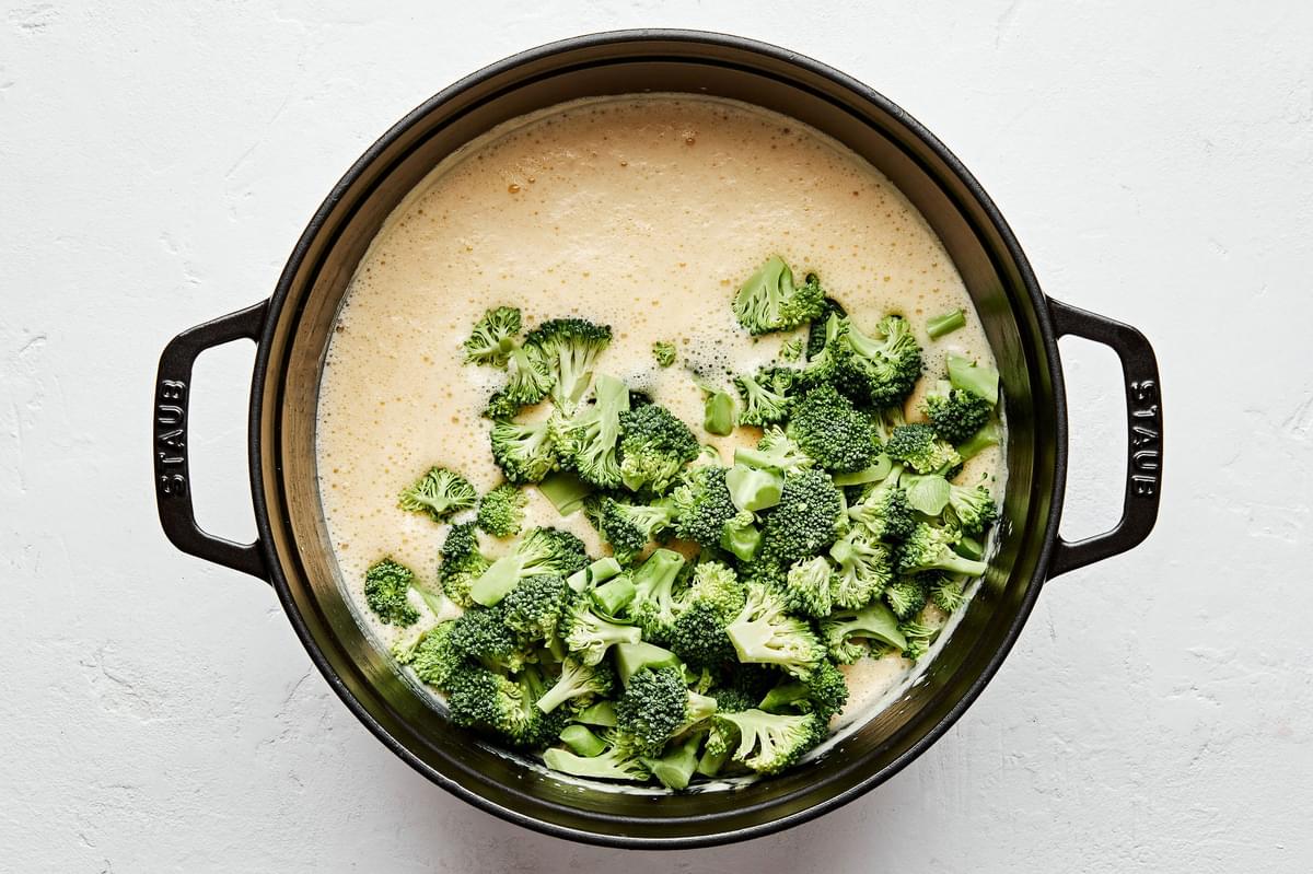 broccoli being added to a pot with blended soup to make broccoli cheddar soup