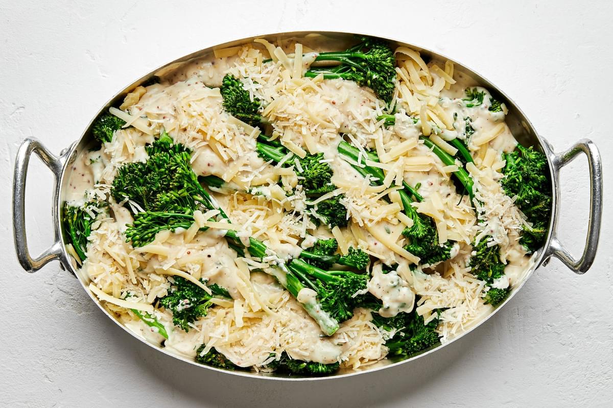 broccolini in a casserole dish covered in cream sauce and topped with Grueyere and Parmesan
