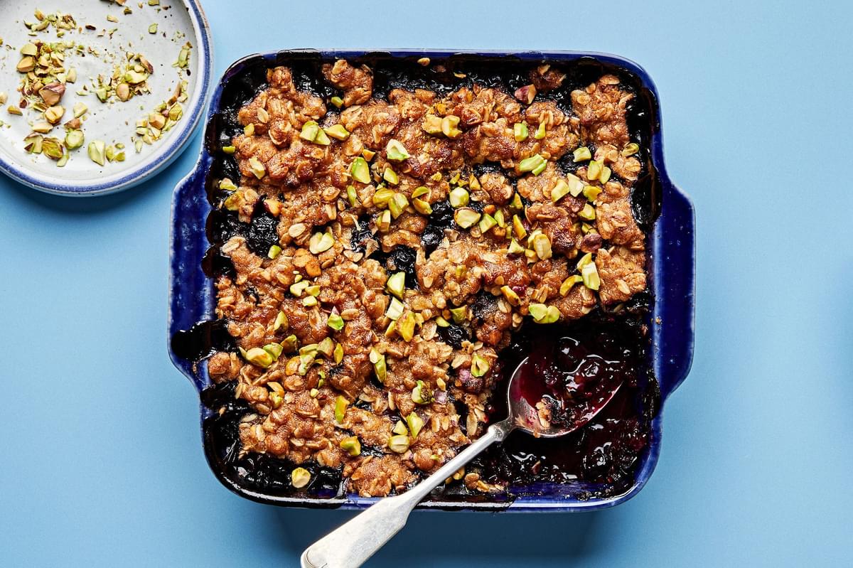 Brown Butter Blueberry Crumble with Pistachios being scooped out of a baking dish with a spoon