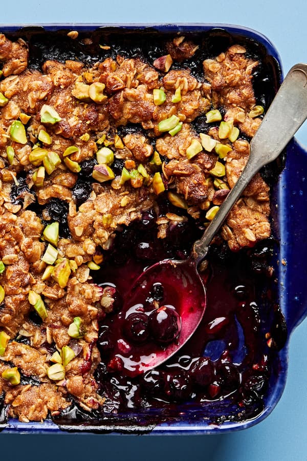 Brown Butter Blueberry Crumble with Pistachios being scooped out of a baking dish with a spoon