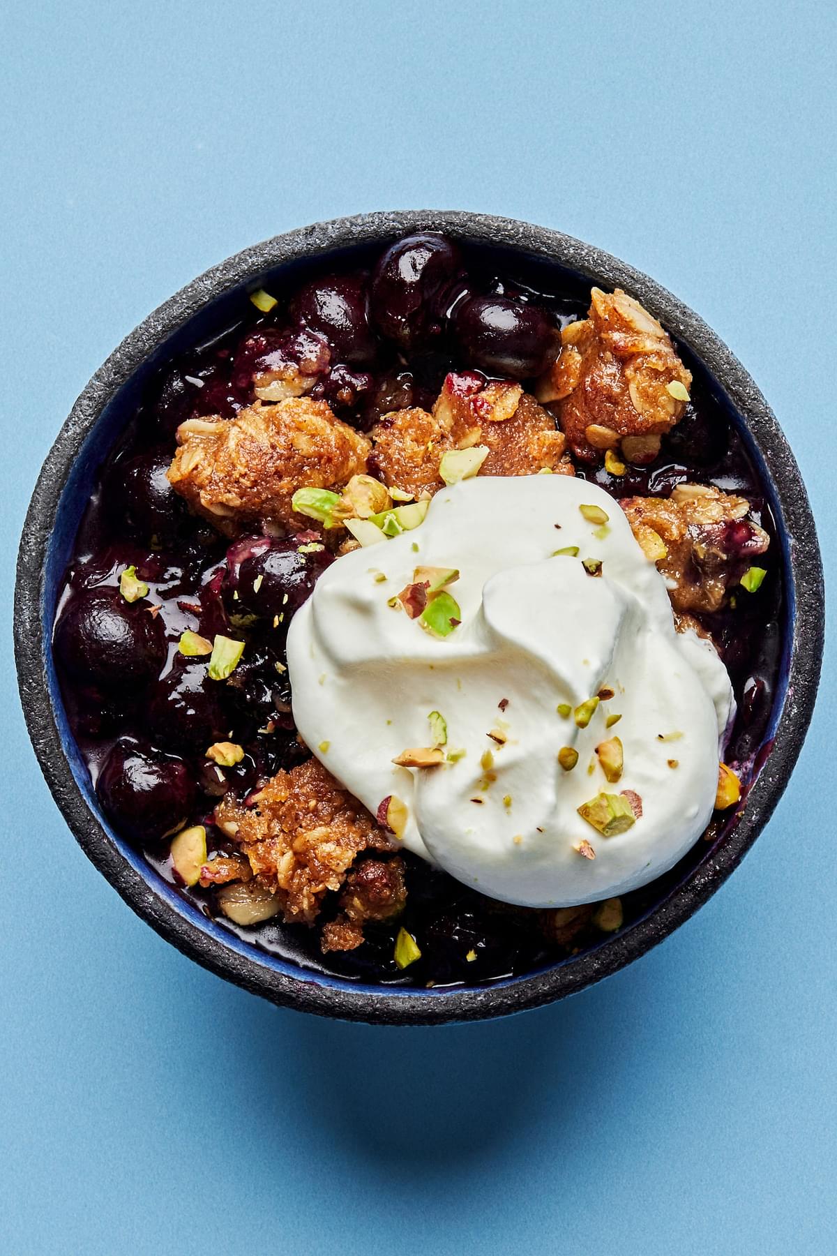 Brown Butter Blueberry Crumble with Pistachios in a bowl topped with a dollop of whipped cream