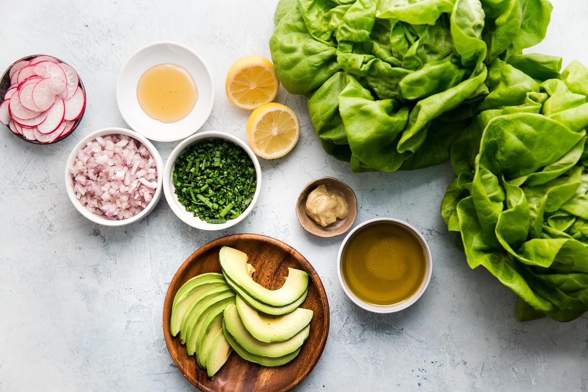 Ingredients laid out for salad bibb lettuce, avocado, radishes, chives, shallots, lemon