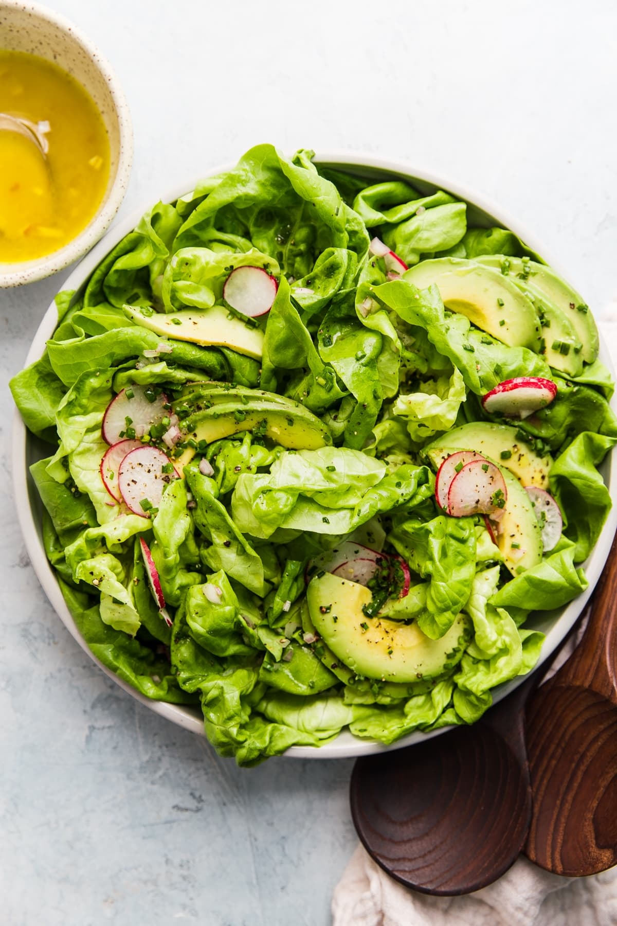 Butter lettuce salad with a honey dijon mustard vinaigrette with radishes, chives, and avocado in a bowl
