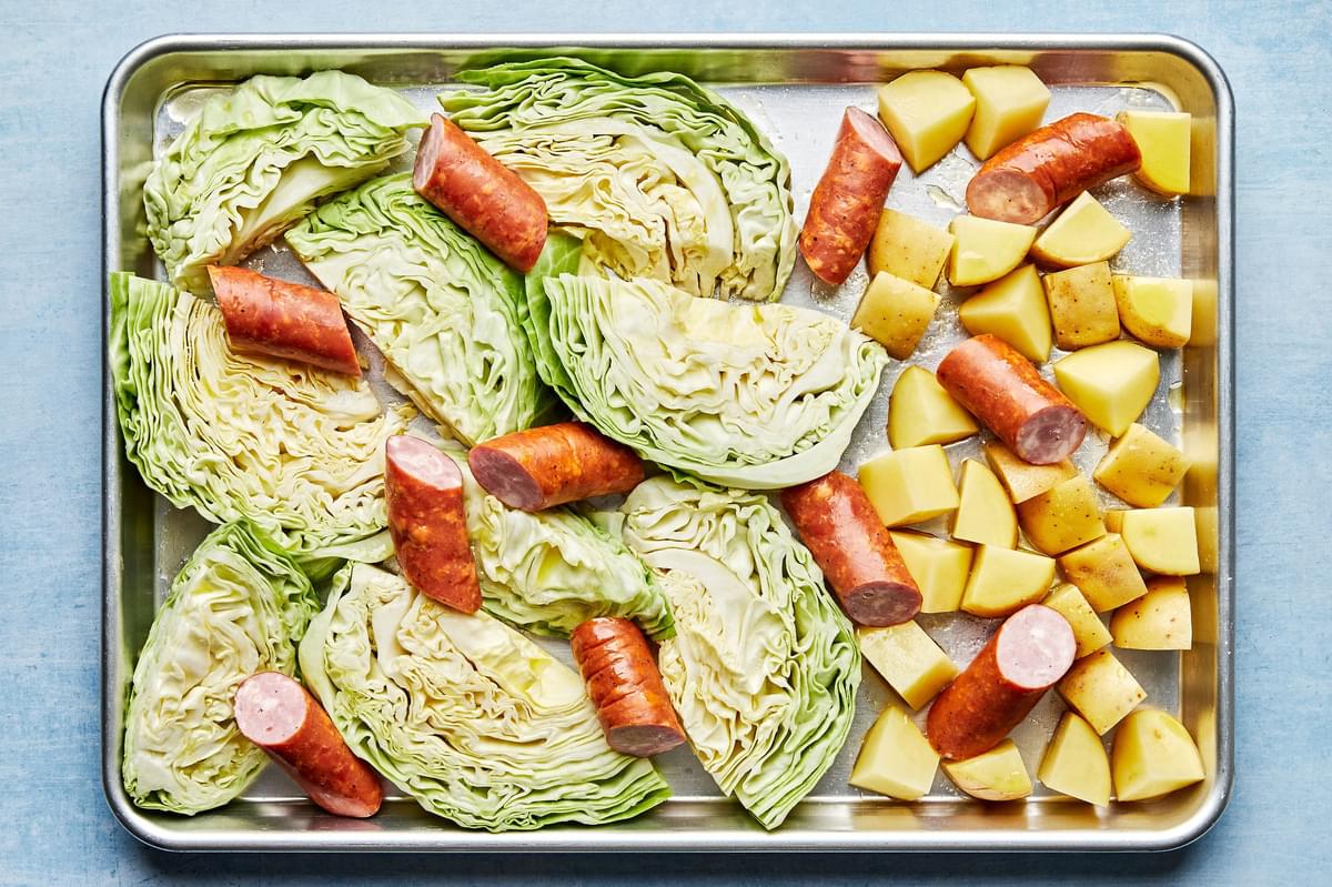 sliced cabbage and potatoes tossed with olive oil and salt on a sheet pan topped with sliced kielbasa sausage